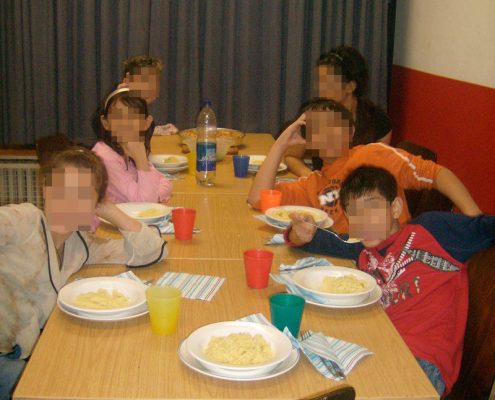 Flüchtlingskinder sitzen um einen Tisch, essen und machen Quatsch.