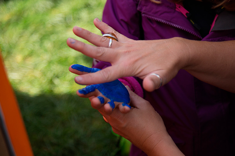 Ein Kind bekommt mit blauer Farbe seine Hand bemalt, um sie auf die Leinwand des Domspitzen eV zu drücken.
